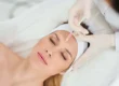 Young woman receives a forehead injection from a gloved professional, lying back with a white headband and towel during Botox and Dysport Treatments in Kenai, AK.